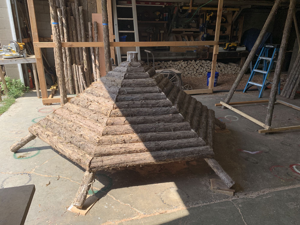 Natural wood covered bench built with trees and branches titled the Fishman Sitting Shelter