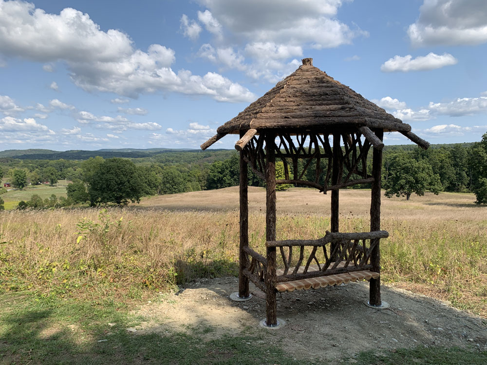 Rustic covered bench custom built using cedar trees and branches titled the Fishman Sitting Shelter