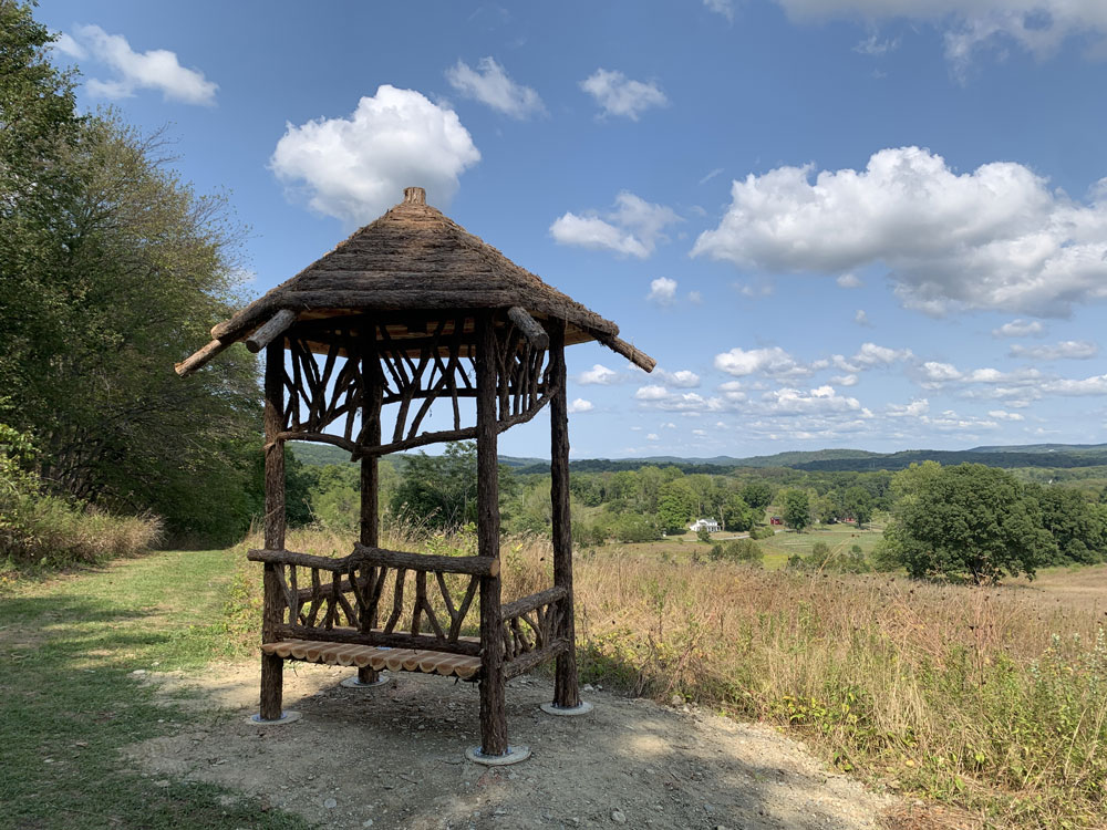 Outdoor rustic covered bench built using bark-on trees and branches titled the Fishman Sitting Shelter