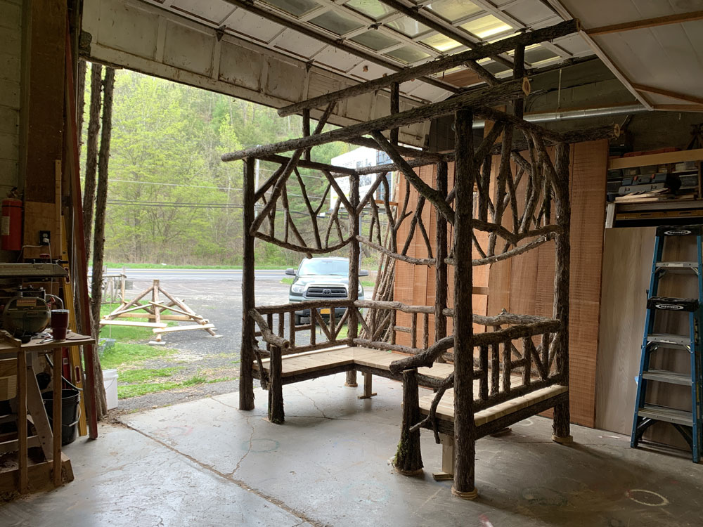 Outdoor sitting shelter built in the rustic style using logs and branches titled the Pachman Shelter