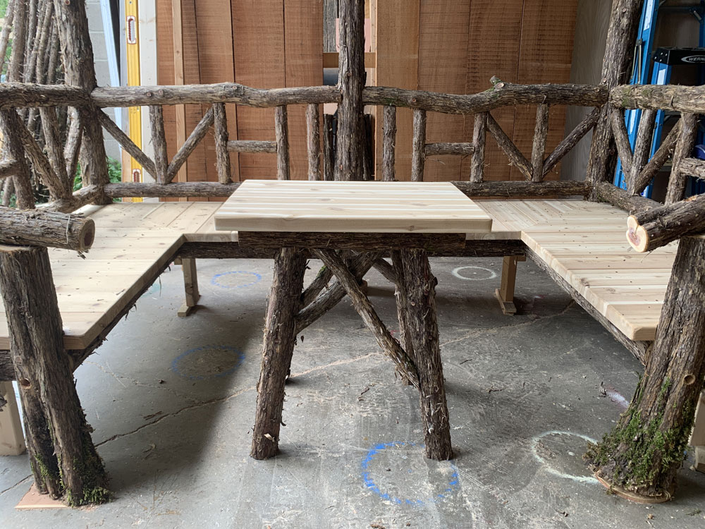 Outdoor rustic sitting shelter built using bark-on trees and branches titled the Pachman Shelter