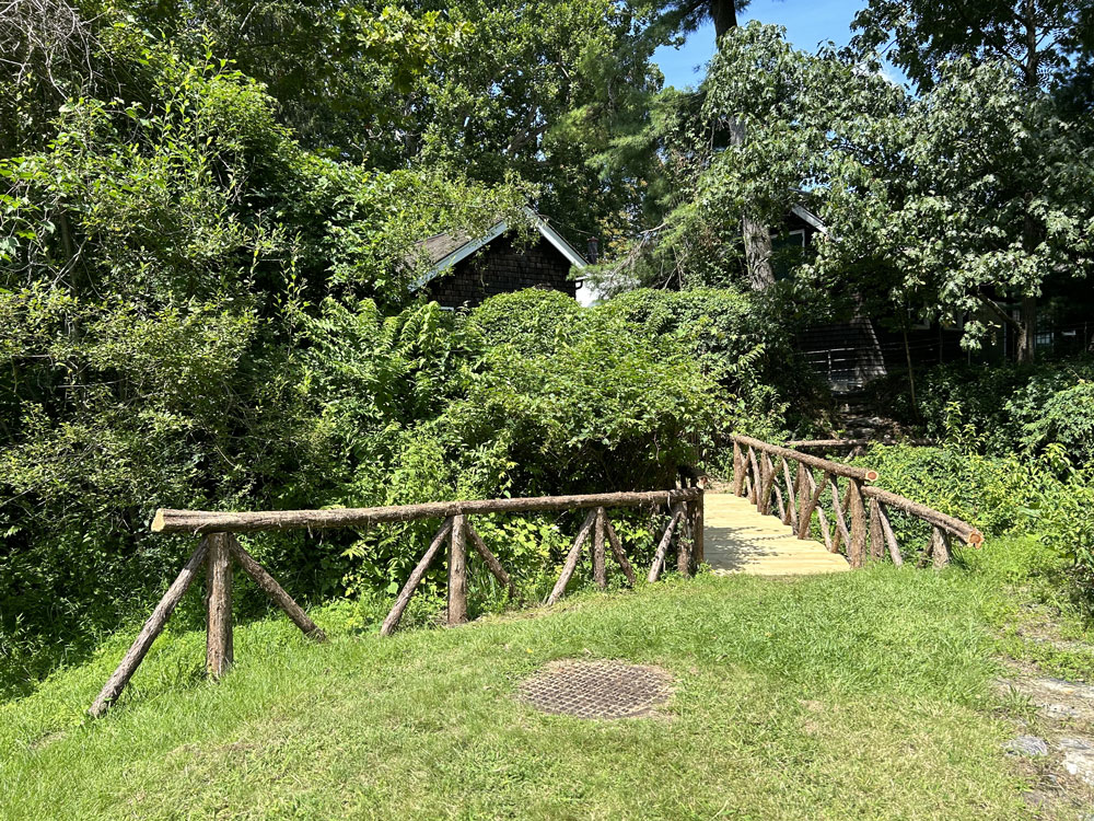 Rustic bridge built using bark-on trees and branches titled the Sunnyside Bridge