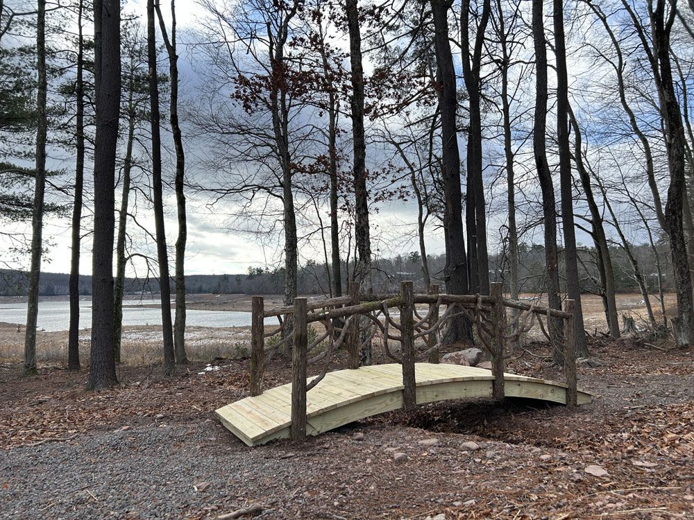 Bridge built in the rustic style using logs and branches titled the White Lake Bridge