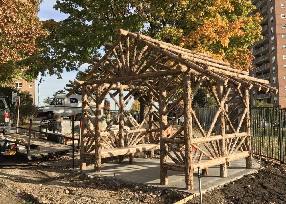 Rustic sitting shelter custom built using cedar trees and branches titled the Skyview Entrance Shelter