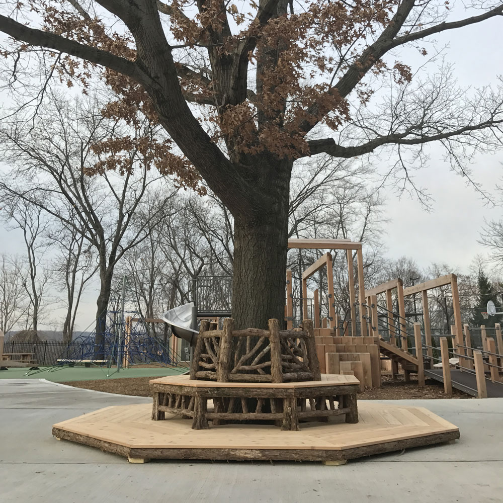 Park bench around a tree built in the rustic style using logs and branches titled the Skyview Tree Bench