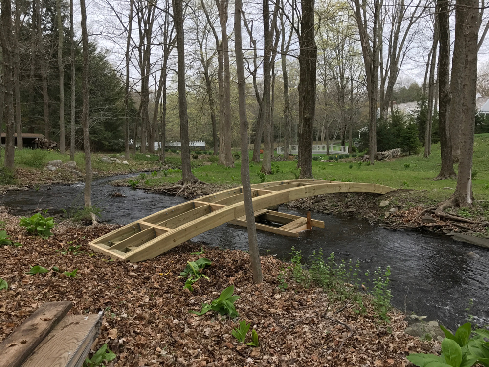 Natural wood bridge built with trees and branches titled the Storm's Crossing