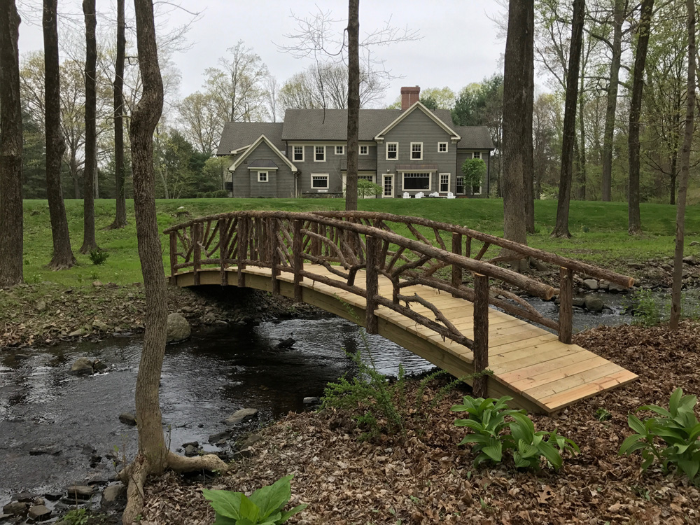 Bridge built in the rustic style using logs and branches titled the Storm's Crossing