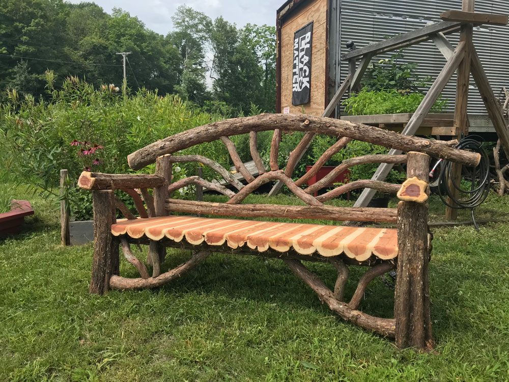 Outdoor rustic garden bench built using bark-on trees and branches.
