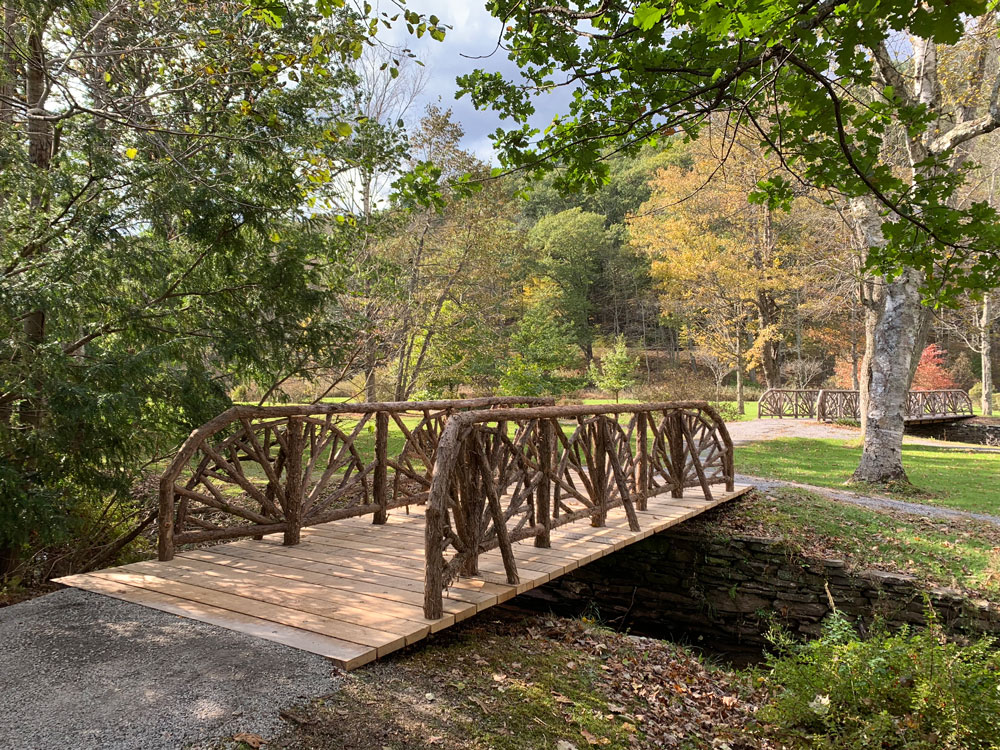 Rustic bridge railings built using bark-on trees and branches titled the Roxbury Bridge at Kirkside Park