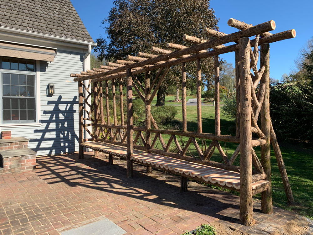 Outdoor rustic covered bench built using bark-on trees and branches titled the Wave Hill Shelter