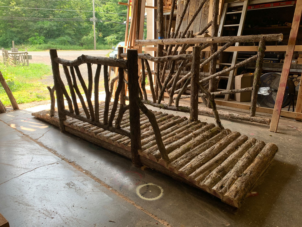 Rustic bridge built using bark-on trees and branches titled the East Branch Bridge