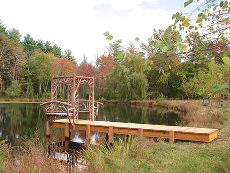 Rustic gazebo and dock built using bark-on trees and branches titled the Williams Dock Shelter