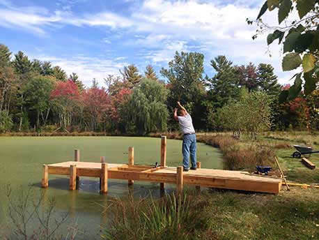 Rustic gazebo and dock built using bark-on trees and branches titled the Williams Dock Shelter