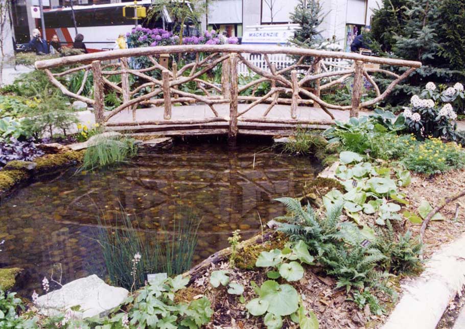 Natural wood bridge over a small pond built with trees and branches titled the Ashokan Bridge