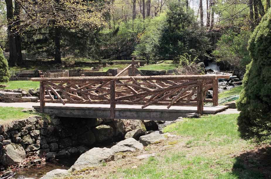 Rustic bridge built using bark-on trees and branches titled the Tuxedo Bridge