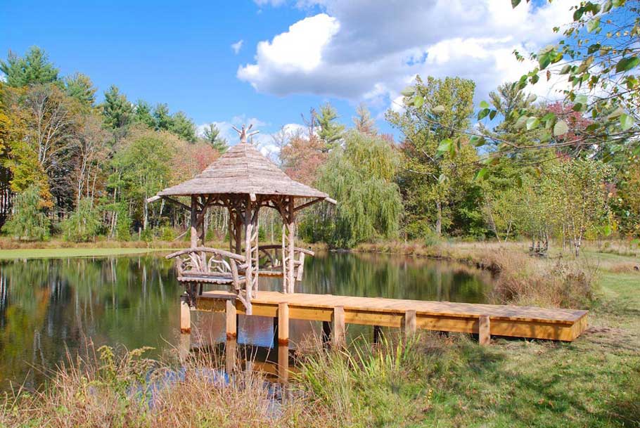 Rustic sitting shelter on the end of a dock built using bark-on trees and branches titled the Williams Shelter