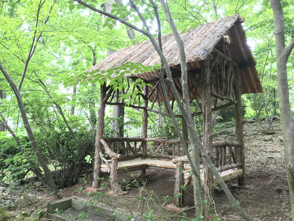 Outdoor rustic covered bench built using bark-on trees and branches titled the Mayhew Shelter