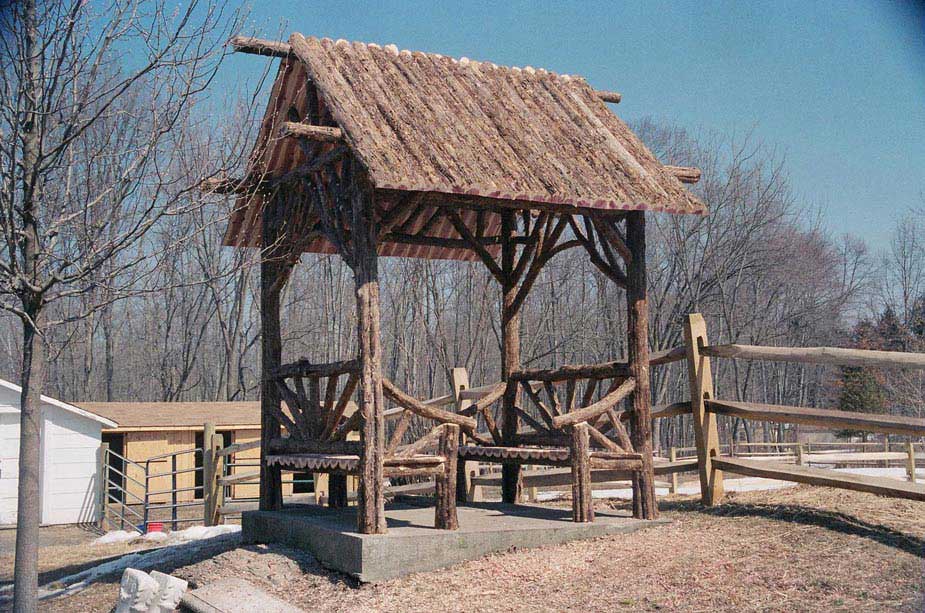 Outdoor rustic covered bench built using bark-on trees and branches titled the Sunburst Shelter