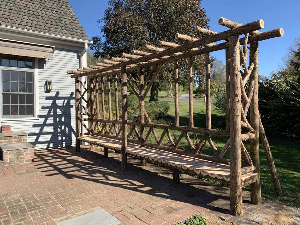 Rustic sitting shelter custom built using cedar trees and branches titled the Wave Hill Shelter