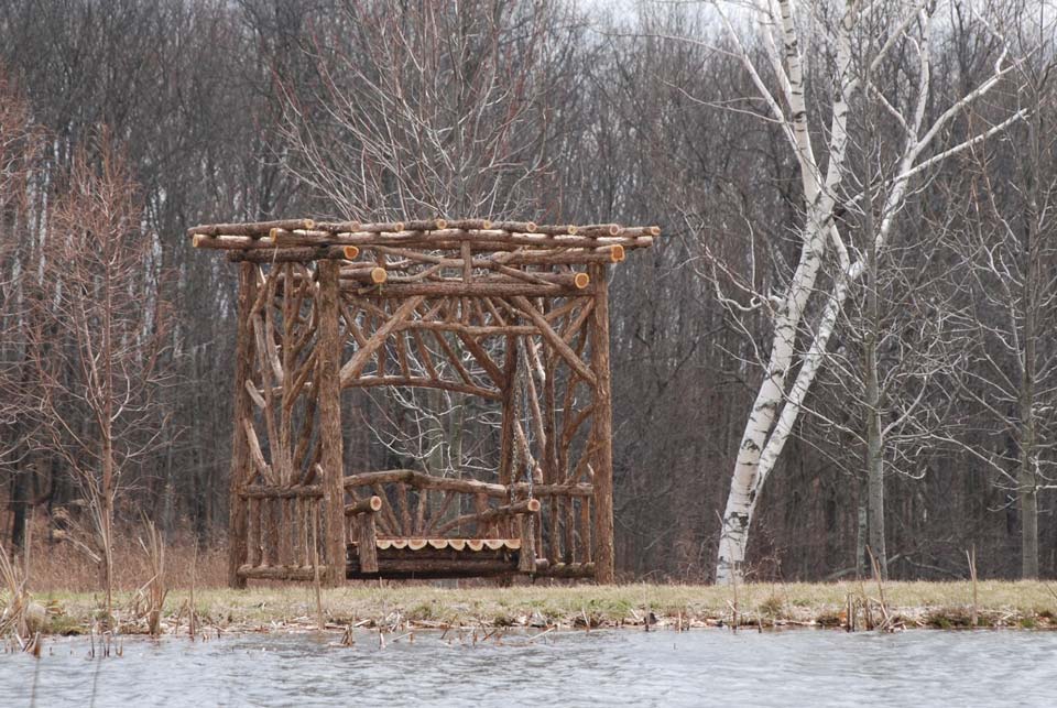 Outdoor rustic bench swing built using bark-on trees and branches titled the Midler Bench Swing
